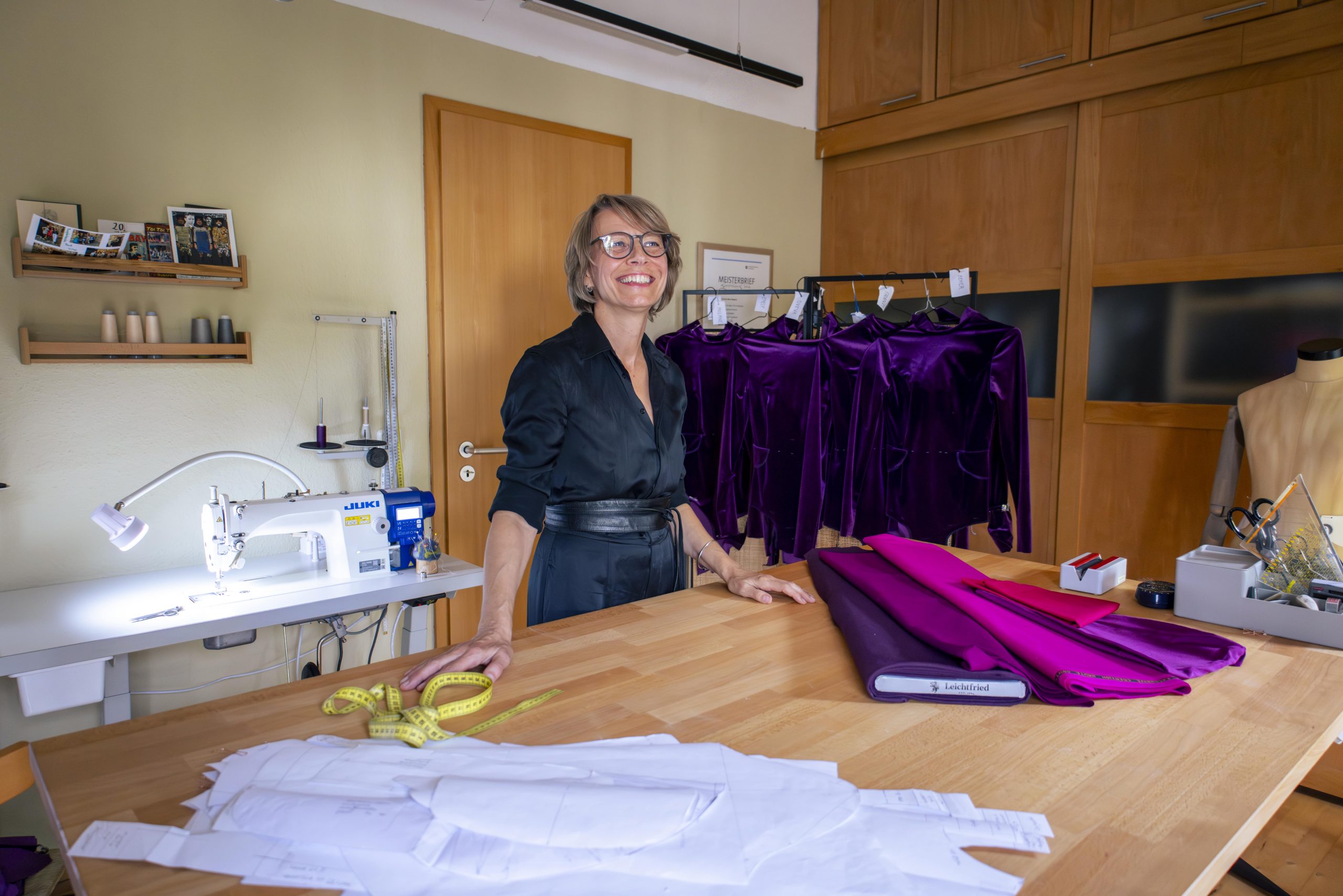 Kordula Magiera in ihrem Atelier, an einem großen Arbeitstisch mit Stoffen, Schnittmustern und Nähmaschine